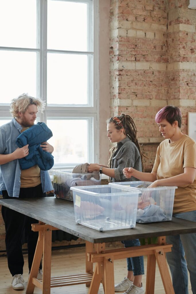 Three volunteers sorting clothes indoors. Engaged in organizing for charity, teamwork, and community service.